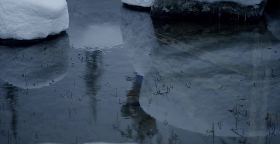 Water in pond reflects person hiking on snow