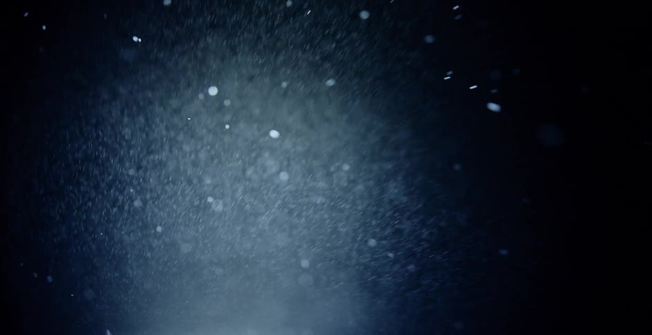 Snow falls towards camera against black background