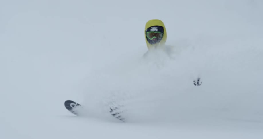 Skier in a yellow jacket skiing down a slope on fresh powder