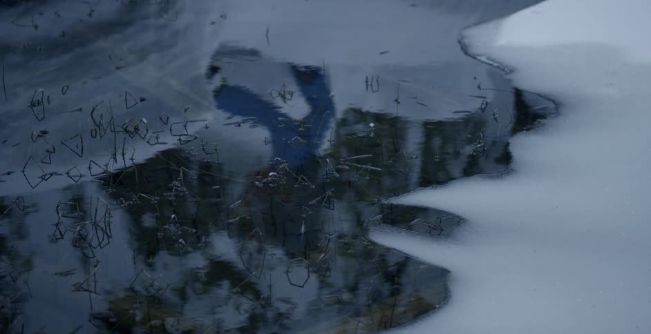 A reflection in a creek of a person walking by on skis