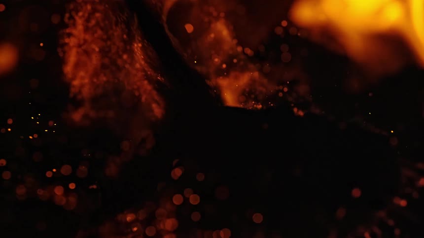 Sparks and embers rise from a burning piece of wood in a fire