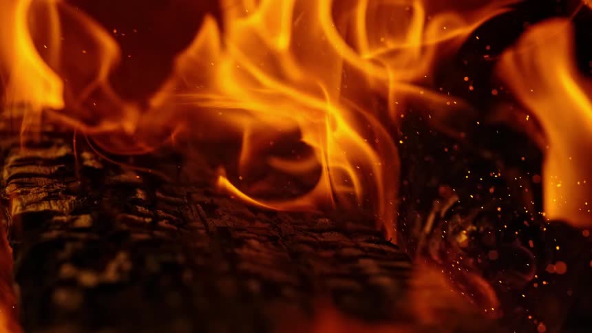 Flames and sparks surround charred wood in slow motion