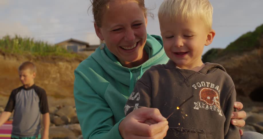 A woman helps a young boy play with a sparkler