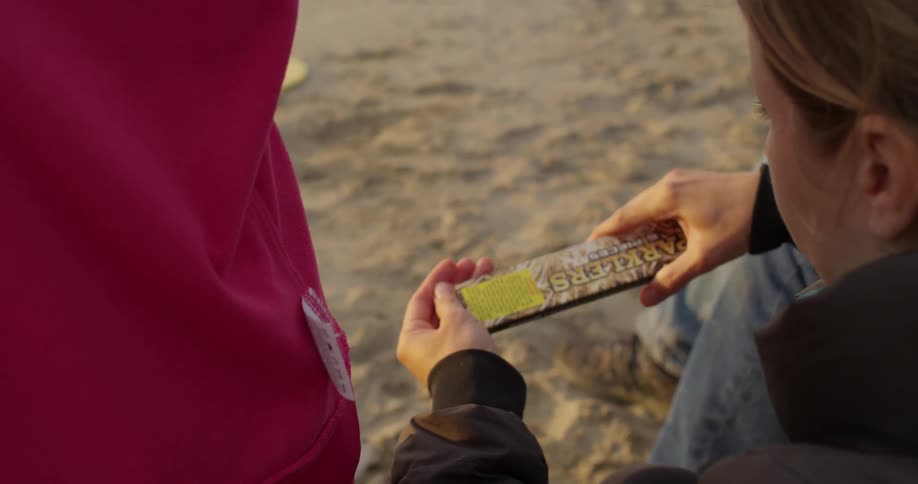 A woman sits in the sand and pours something from a package into her hand