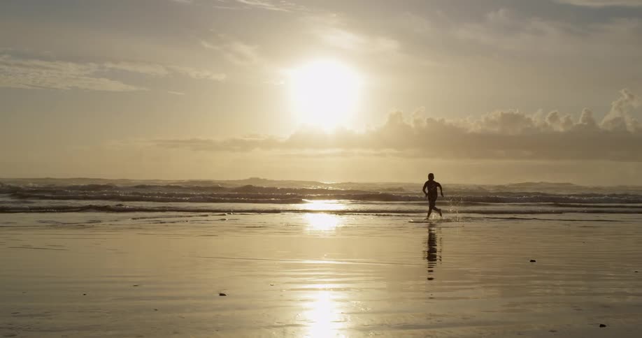 A boy plays with a board in the surf at sunset
