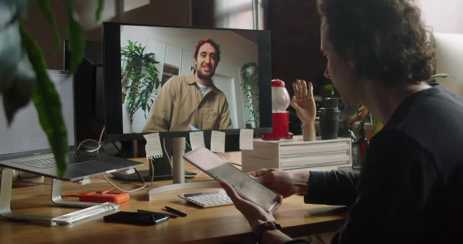 Man uses tablet while having video conference on desktop computer