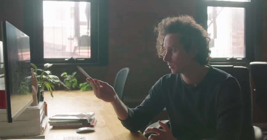 Man sitting at the table uses tablet and makes a video call on the desktop in the office