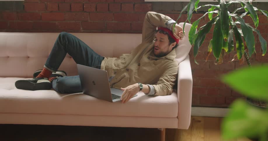 A white man lies on a couch while talking to someone through a laptop computer