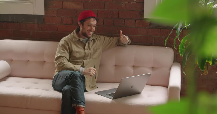 Man sits on couch against brick wall having teleconference