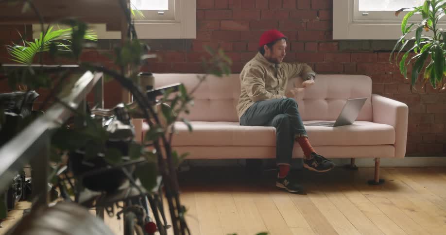 Man teleconferences while sitting on couch near windows