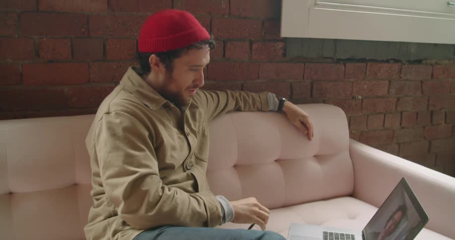 A man sitting on a sofa using a laptop to video chat with another man