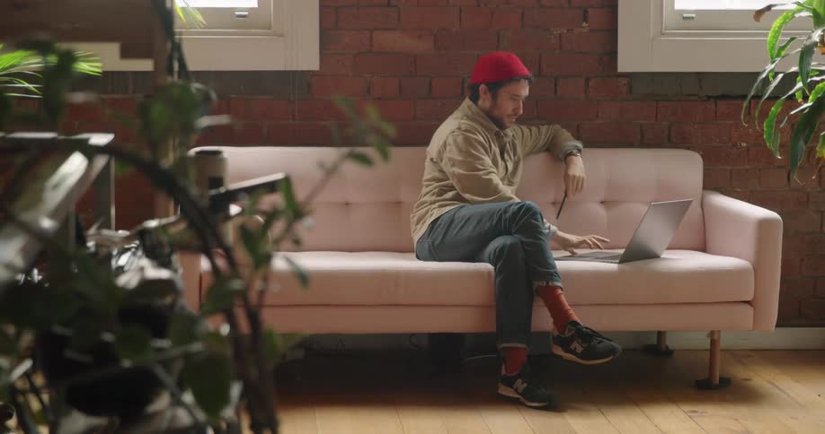 Man sitting on couch in living room opens laptop and smiles