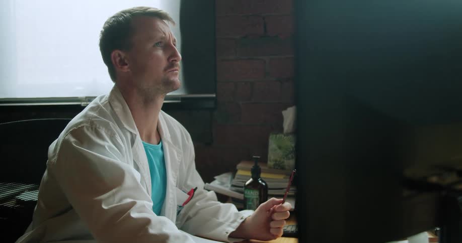 Doctor sits at desk reviewing computer monitors