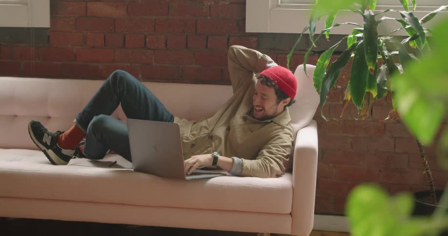 A person lays on a couch looking at a laptop