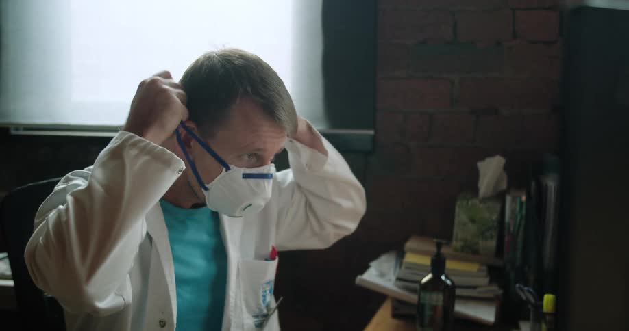 A man in a lab coat puts on a ppe mask