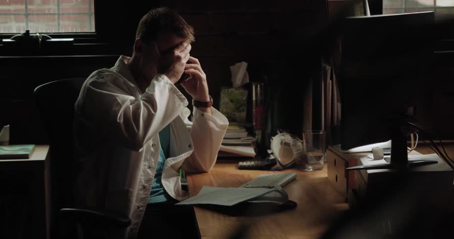 Man sits at desk talking angrily on phone in darkened room