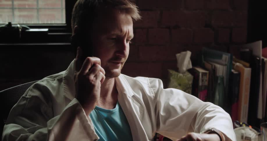 A doctor talks on a cell phone while writing on a paper then looks at his watch and gets up to leave the room