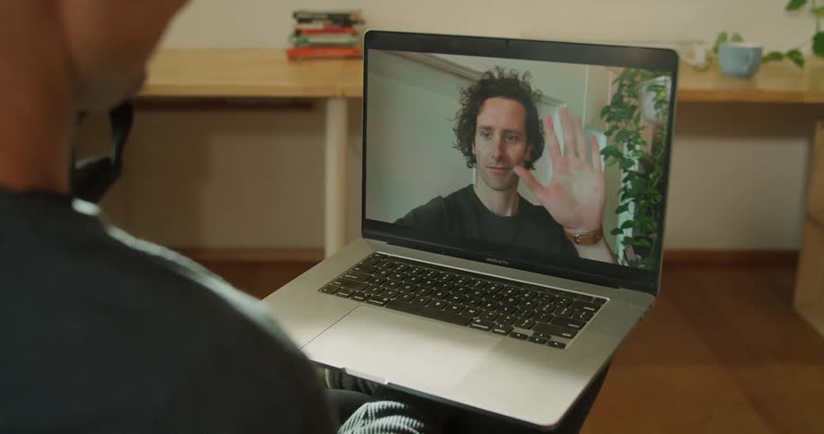 Two men wave at one another through a laptop
