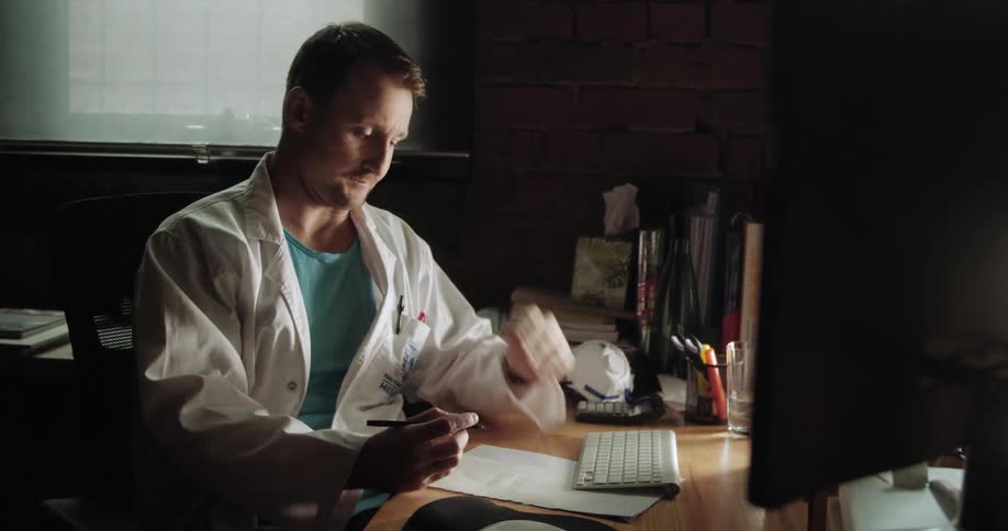 A man sits at his desk rubs his forehead and writes on a paper
