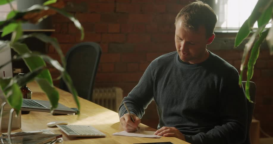 Man sitting at the table skypes on the laptopand takes notes in the office building