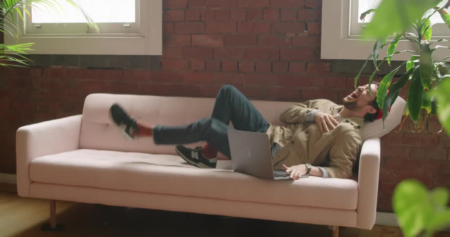 Man making a video call on the laptop bursts into laughter in the room