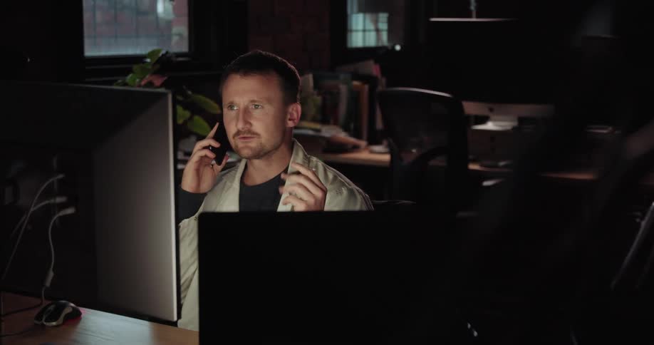 A doctor talks on a cell phone while looking at a computer screen in a dark office