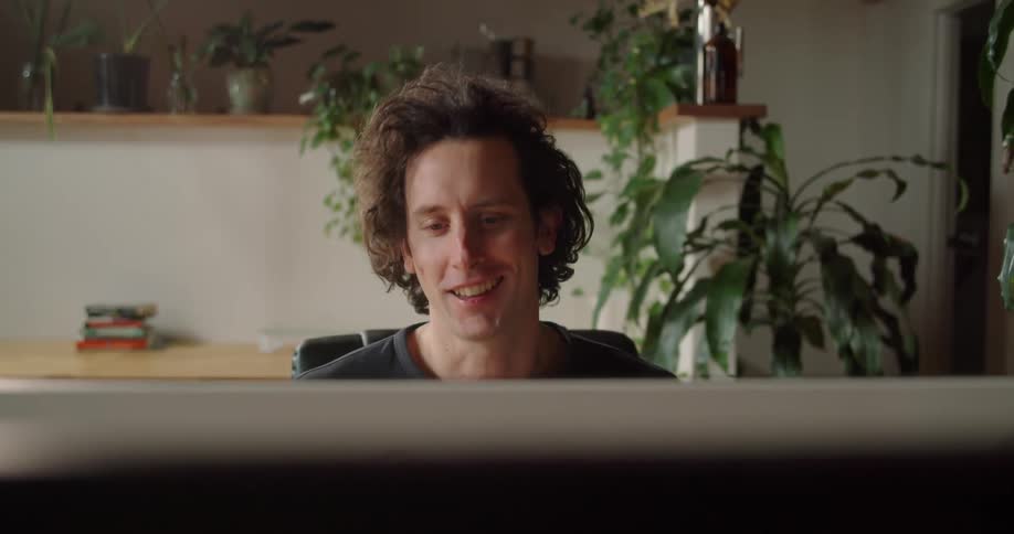 Man sitting at the table uses a laptop and talks to someone in the office
