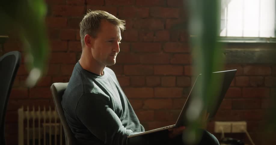 A man sitting in a chair using video chat on a laptop