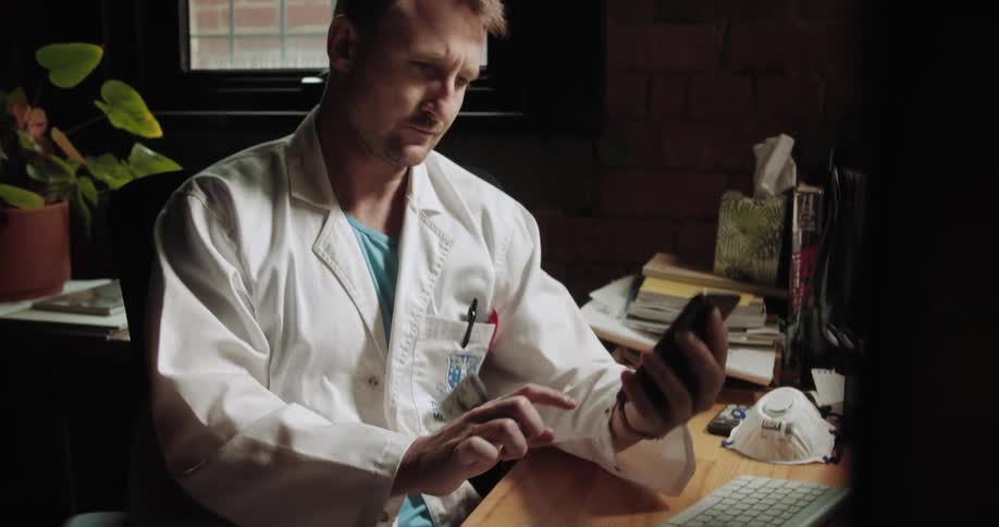 A man in a lab coat texts on a cell phone