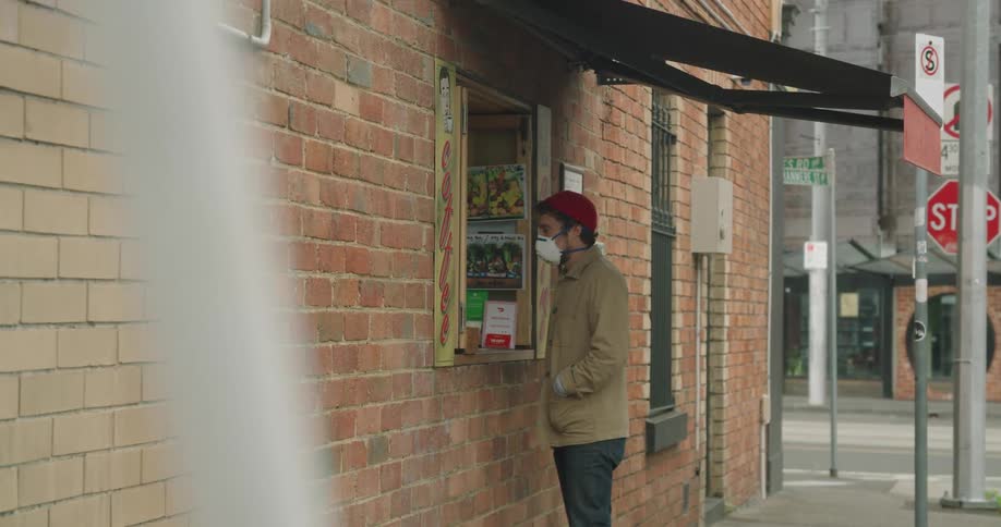 A man wearing a mask walks up to a window on a street