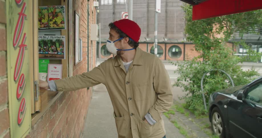 A man wearing a face mask picks up a drink from a cafe