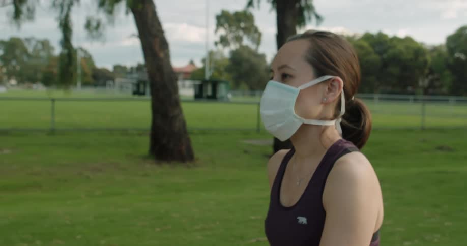 A woman wearing a surgical mask walks through a park