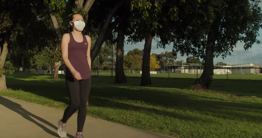 Woman wearing mask jogging in park at sunrise