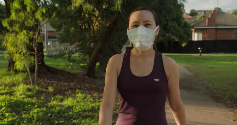 A woman wearing a medical mask walks down a path through a park