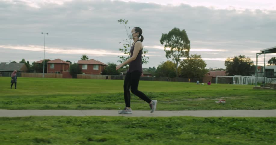 Woman walks along path in park wearing mask