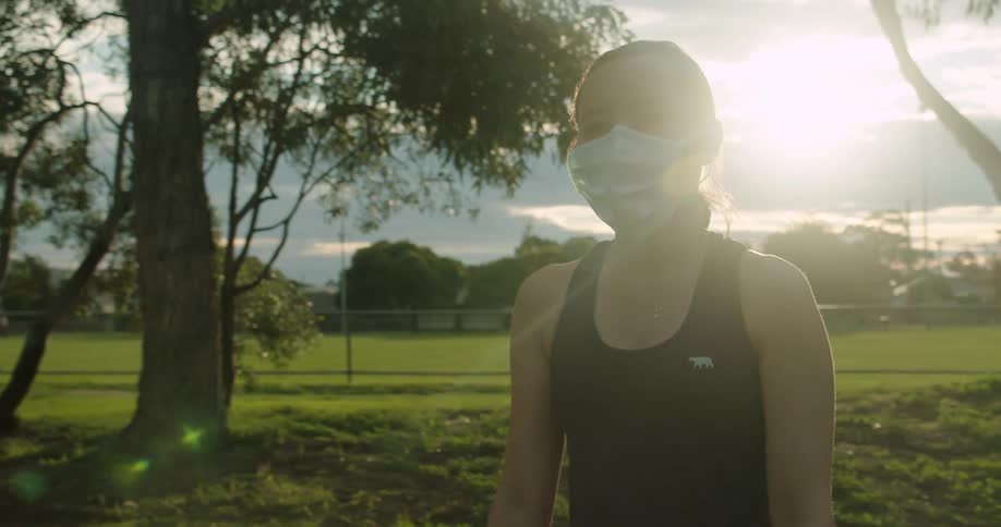A woman walking with a mask on with a field in the background
