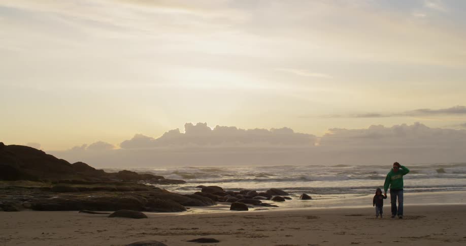 A man walks with a young child on a beach at dawn