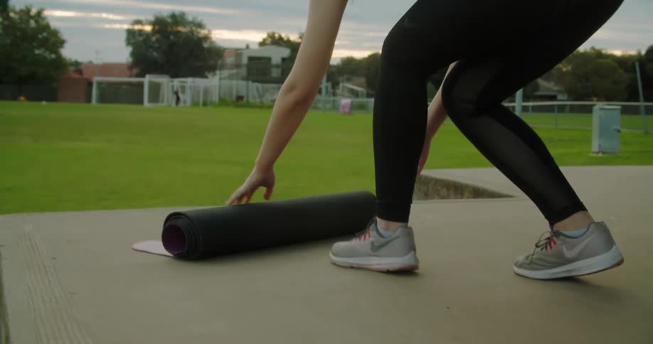 Woman rolling out yoga mat on band shell flooring at a park