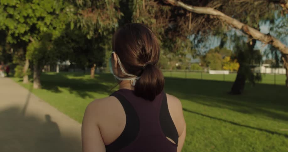 A woman wearing a surgical mask walks on a path through a park