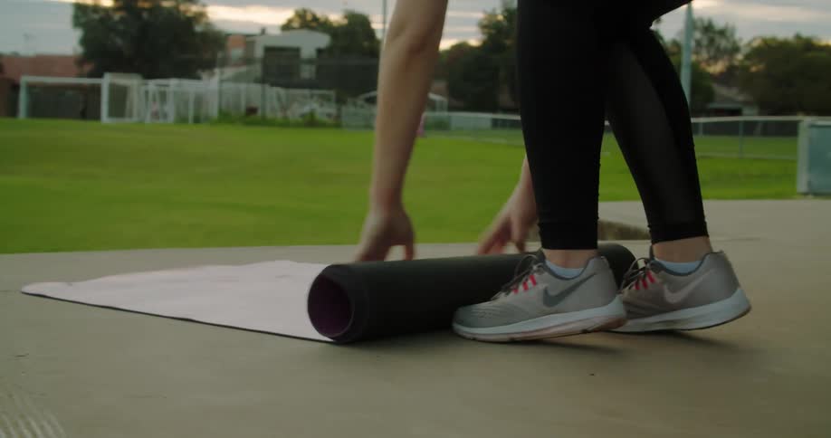 Woman rolls out yoga mat on pavement near fields