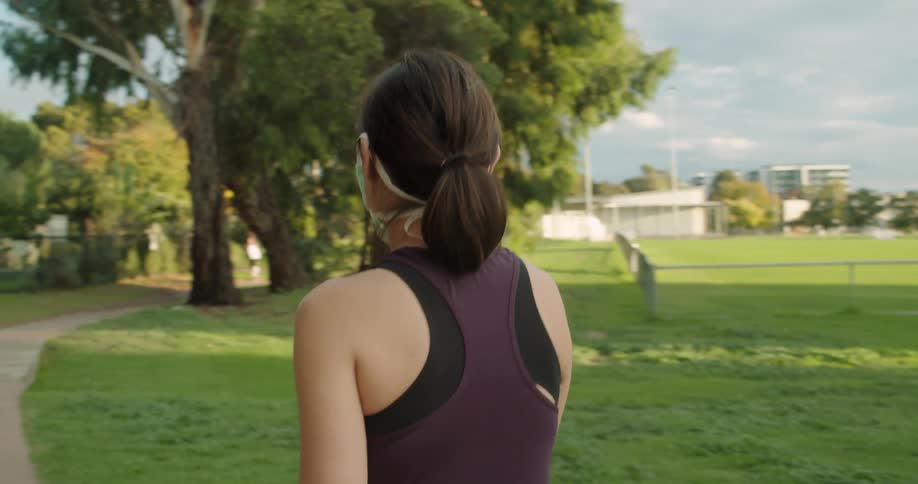 A woman wearing a mask walks through a path in an empty park