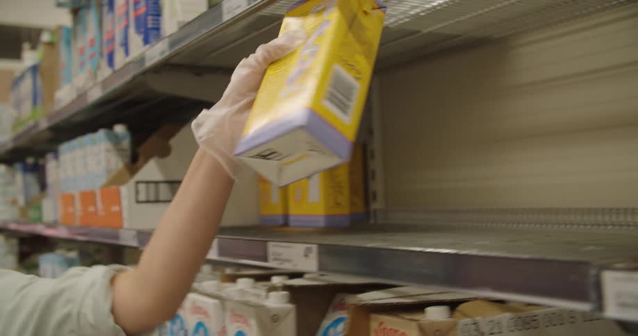 A woman wearing a mask takes an item off of a grocery shelf