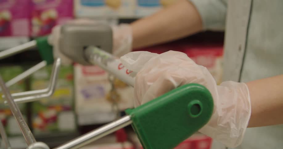 A shopper pushes a shopping cart in a store while wearing latex gloves
