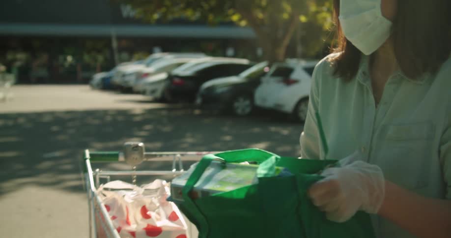 A woman wearing a medical mask loads groceries from a shopping cart into her car