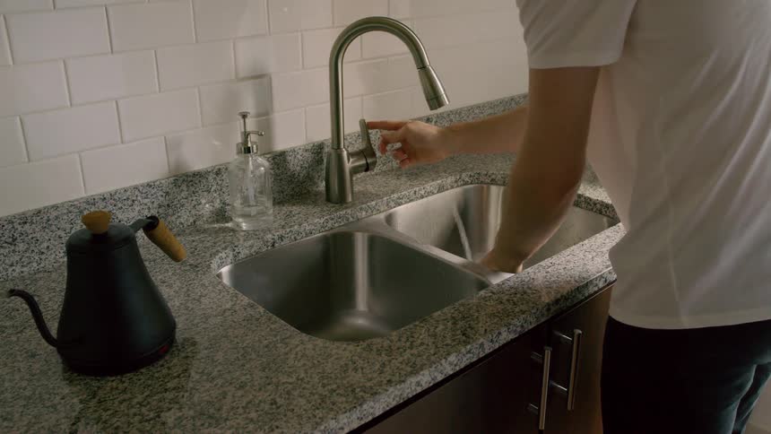 A man washes his hands in his kitchen sink