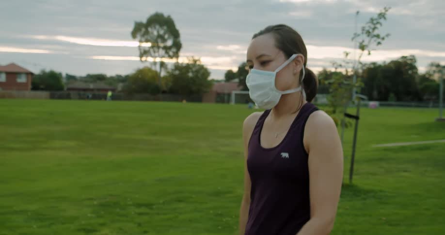 A woman walks through a grassy field while wearing a face mask