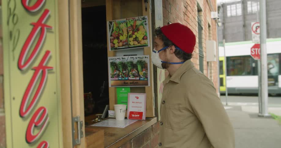 A man with a mask places an order at a window on a street