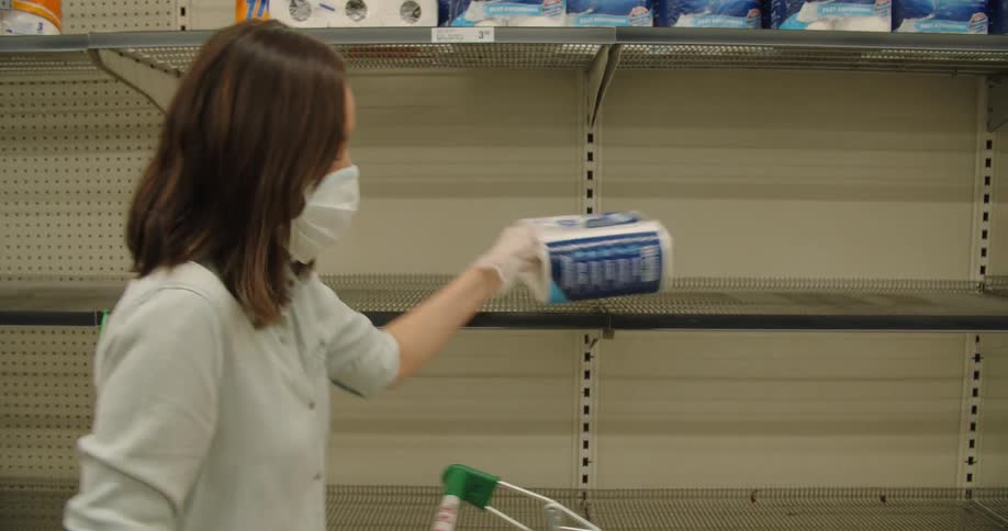 A woman wearing a medical mask and gloves takes the last item from a store shelf