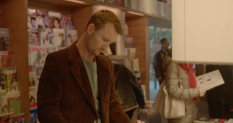 A man picks up a book and starts flipping through the pages while standing in a store with other customers