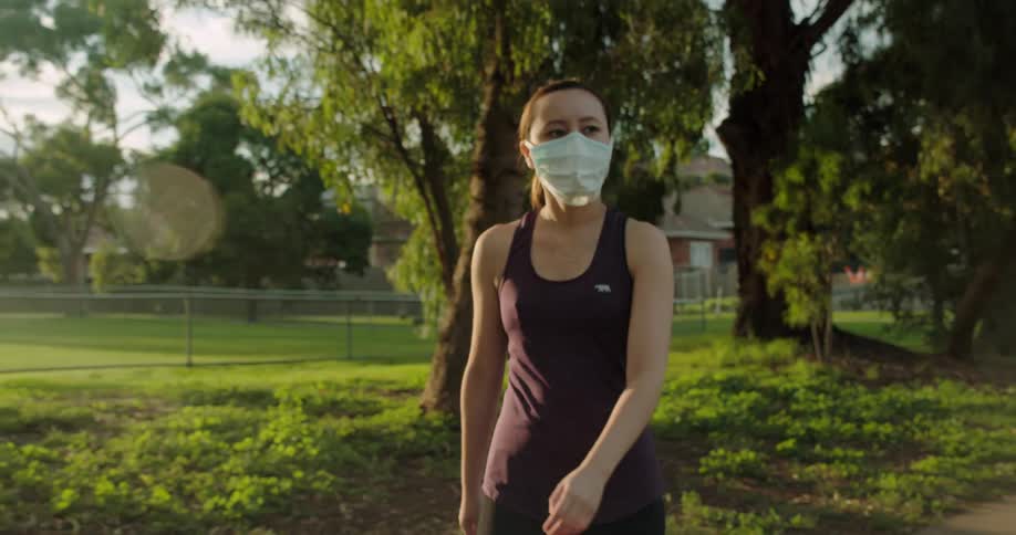 Woman wearing face mask and athletic clothing walks down empty sidewalk